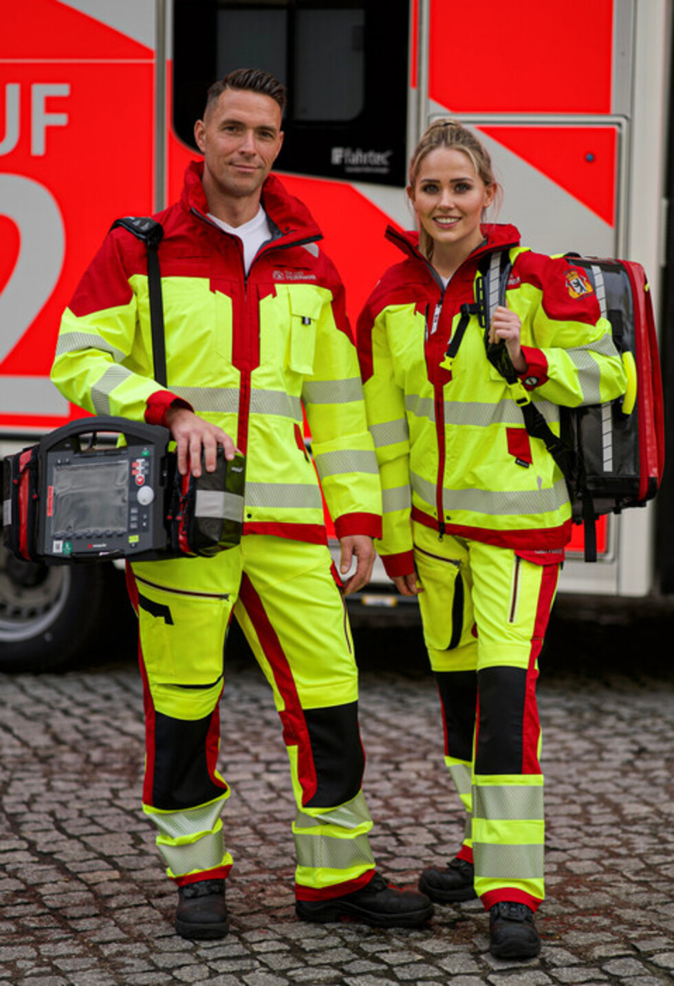 2 Personen stehen in Schutzkleidung vor einem Rettungswagen